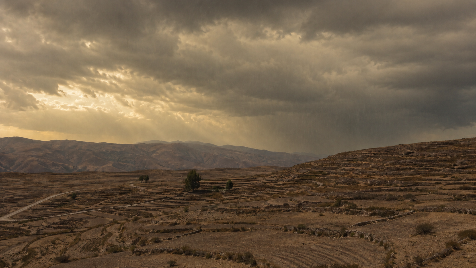 An arid terraced hillside under heavy cloud, empty of people.
