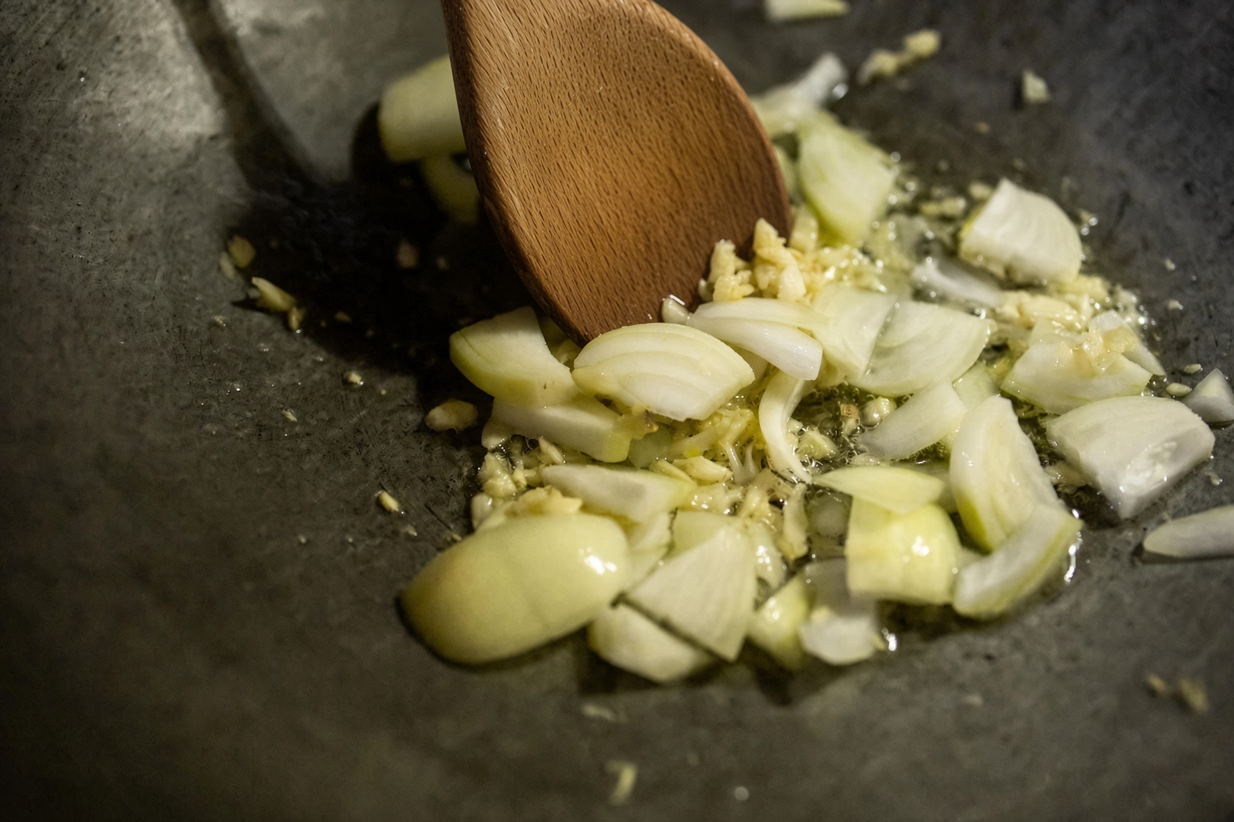 Onion and garlic softening in the pan under a wooden spoon